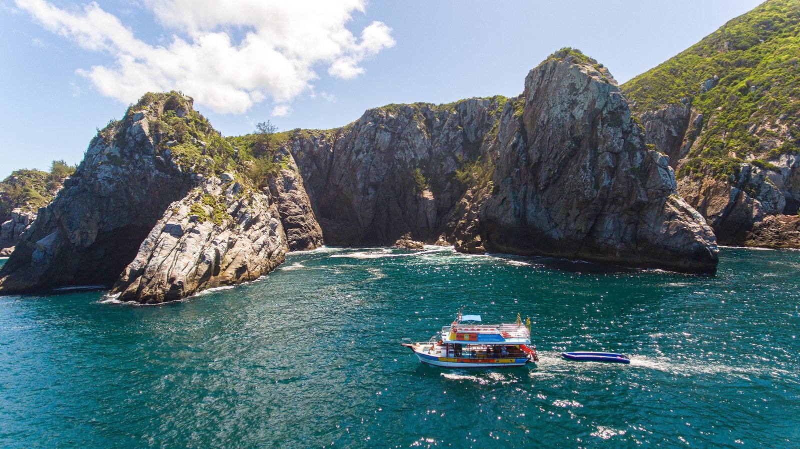 Barco da Kiko Tour navegando junto aos paredões de pedra do mar de fora de Arraial do Cabo